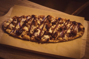 Pulled Pork flat pizza served on a wooden tray at the Legendary Axe Throwing Detroit.